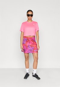 Ροζ κοντό τοπ με κοντά μανίκια, συνδυασμένο με φούστα σε μοτίβο λουλουδιών σε μοβ και ροζ αποχρώσεις. Μαύρα αθλητικά παπούτσια και γυαλιά ηλίου ολοκληρώνουν την εμφάνιση.