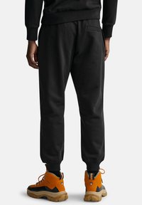 Czarne dresy z elastycznym pasem, zwężonymi nogawkami i tylną kieszenią, zestawione z pomarańczowo-czarnymi butami trekkingowymi.