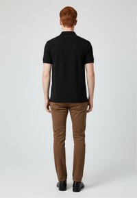 Černá polo triko s krátkým rukávem, hladkým materiálem a límečkem, spárované s hnědými slim-fit kalhotami a černými botami.