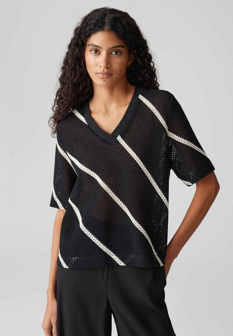 Top corto a maniche corte in rete nera con scollatura a V, caratterizzato da strisce diagonali bianche. Il tessuto è leggero con un motivo a trama aperta.