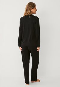 Sort langærmet top og matchende bukser i blødt stof. Outfittet har en afslappet pasform med en glat tekstur og minimal detaljering.