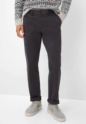 Dunkelgraue Chinos aus Baumwolle mit glatter Textur und taillierter Passform, kombiniert mit aufgerollten Säumen und grauen Sneakern.