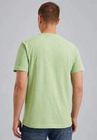 T-shirt en coton vert clair avec des manches courtes, un col rond et une coupe légèrement décontractée, vu de dos. Un jean bleu est visible en dessous.