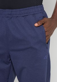 Granatowe dresy wykonane z teksturowanej tkaniny, z elastycznym pasem, bocznymi kieszeniami i dyskretnym logo na dolnej części nogawki.