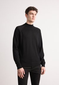 Pull noir à col rond avec des manches longues, poignets et ourlet côtelés, présentant une texture lisse et des détails discrets aux coutures des épaules.
