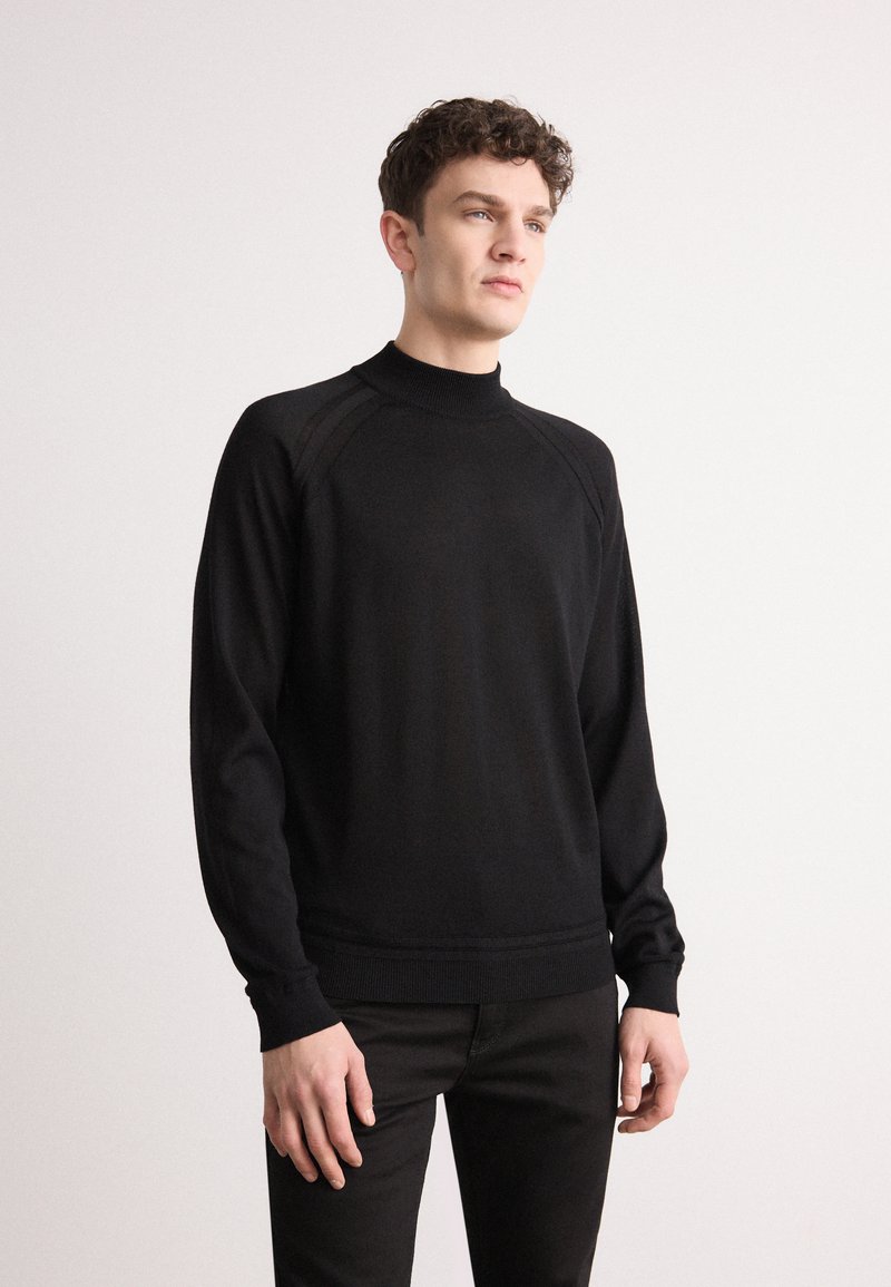 Pull noir à col rond avec des manches longues, poignets et ourlet côtelés, présentant une texture lisse et des détails discrets aux coutures des épaules.