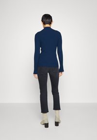Navy ribbed turtleneck sweater paired with dark jeans. Model shows back view, featuring long sleeves and a fitted silhouette.