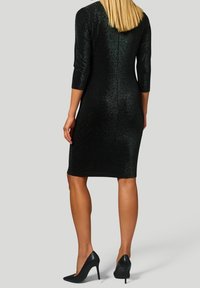 Svart, glittrande knälång klänning med trekvartsärmar, figurnära design och dragkedja bak. Bärs med svarta högklackade skor.