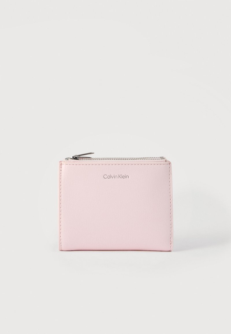 Ανοιχτό ροζ πορτοφόλι Calvin Klein με φερμουάρ στην επάνω πλευρά και ορατό λογότυπο της μάρκας στο κεντρικό μπροστινό μέρος.