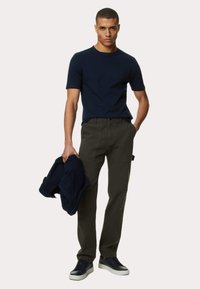 Námořnické tričko, olivové cargo kalhoty a námořnická bunda držena v ruce. Model má na sobě námořnické tenisky. Casuální outfit se bočními kapsami.