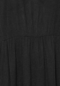 Tissu noir avec une couture froncée créant des plis doux et une texture dans un matériau léger et fluide.