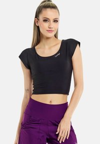 Sort cropped t-shirt med rund halsudskæring og korte ærmer, prydet med et diskret hvidt logo. Bæres sammen med højtaljede lilla træningsbukser.