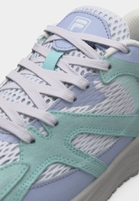 Κοντινό πλάνο ενός λευκού και ανοιχτού γαλάζιου αθλητικού παπουτσιού με σουέντ επικαλύψεις σε χρώμα μέντας, λευκά κορδόνια, επάνω μέρος από δίχτυ και ετικέτα με τη μάρκα στη γλώσσα.