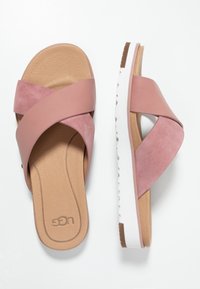 Pink suede cross-strap sandals with a cushioned tan insole and a white sole. Features a textured footbed and a comfortable, flat design.