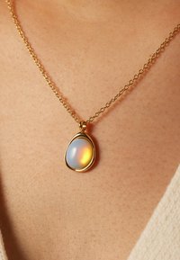 Gouden ketting met een ovale opaal hanger met een glad oppervlak dat iriserende blauw- en oranje tinten toont.