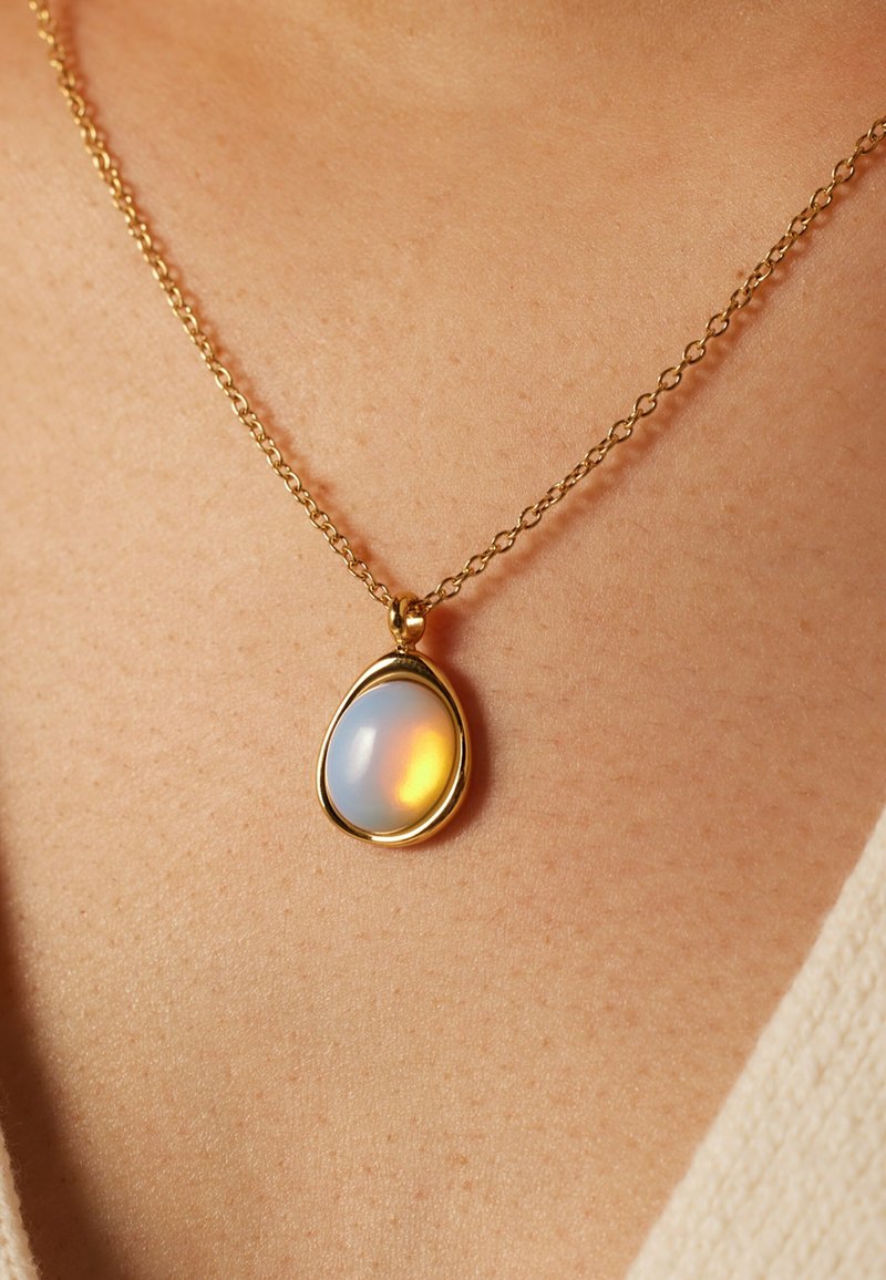 Gouden ketting met een ovale opaal hanger met een glad oppervlak dat iriserende blauw- en oranje tinten toont.