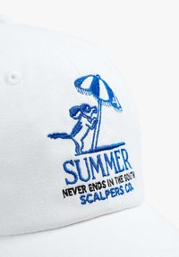 Gorra de béisbol blanca con gráficos bordados azules de un perro, una sombrilla de playa y el texto: “EL VERANO NUNCA TERMINA EN SOUTH SCALPERS CO.”