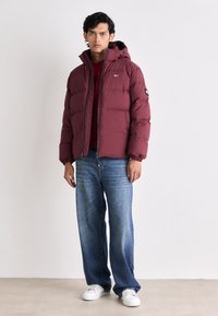 Burgundy puffer jacket with a hood, zip closure, and elastic cuffs, paired with light blue wide-leg jeans and white sneakers.