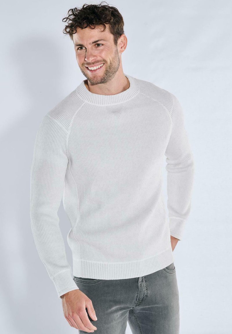 Weißer gerippter Pullover mit langen Ärmeln und Rundhalsausschnitt, aus einem strukturierten Material, kombiniert mit grauen Jeans.