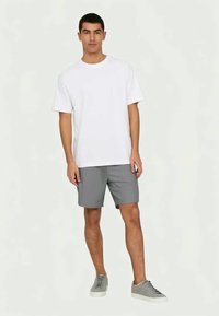 T-shirt en coton blanc, coupe décontractée, associée à un short gris. Des baskets grises complètent la tenue, mettant en avant un style décontracté.
