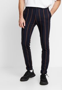 Navy striped trousers with vertical brown lines, slim fit design, and a flat front. Paired with black sneakers and white socks.