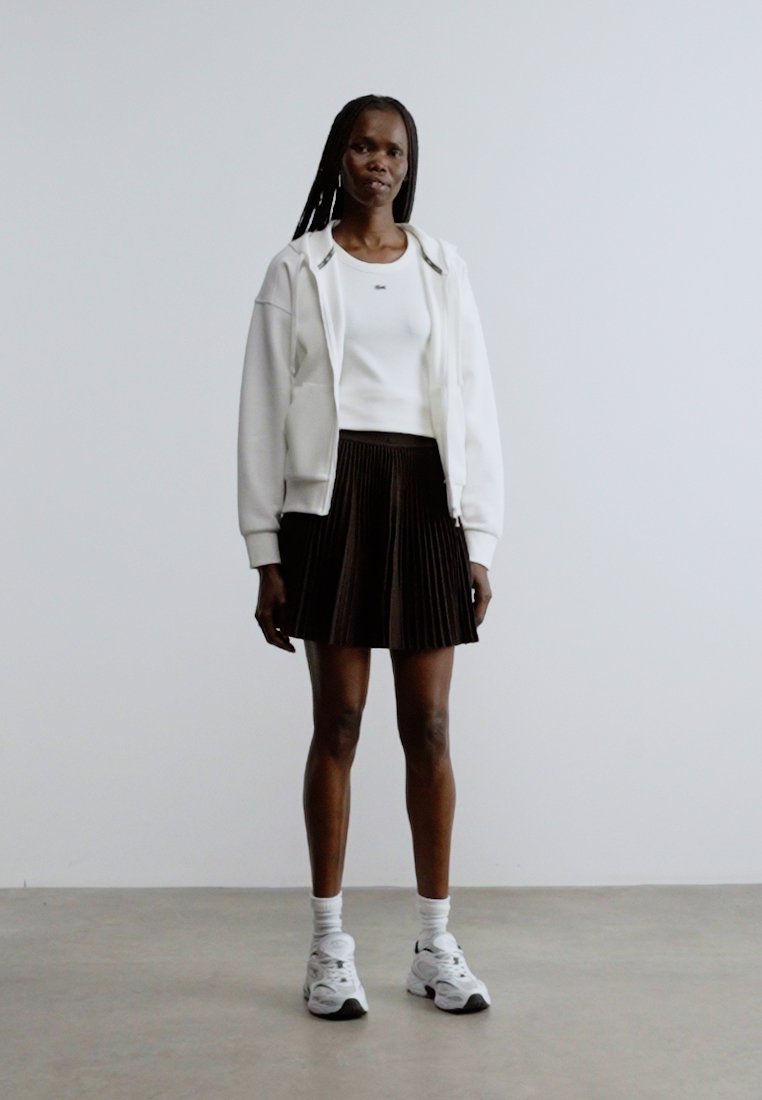 Hoodie blanc zippé, haut blanc ajusté, jupe plissée marron, chaussettes blanches et baskets blanches épaisses. Texture lisse et design décontracté.