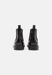 Black leather ankle boots with elastic side panels, round toe, and pull tabs at the back. Smooth texture and flat rubber sole.