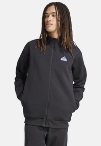 Zwarte zip-up sweatshirt met een hoge kraag, gemaakt van gladde stof, heeft een blauw Adidas-logo op de linkerkant van de borst. Lange mouwen en geribde manchetten.