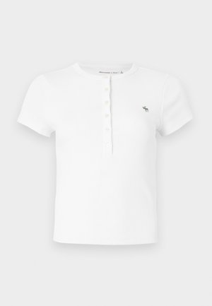 Vit kortärmad ribbad t-shirt med rund halsringning och knappslå, med en liten grön broderad logotyp på vänster bröst.