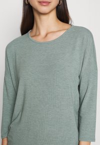Vaalea vihreä pitkähihainen paita, jossa on pyöreä pääntie ja väljä malli. Pehmeä, tekstuuriainen kangas, jossa on laskettu olkaimekko ja rento siluetti.