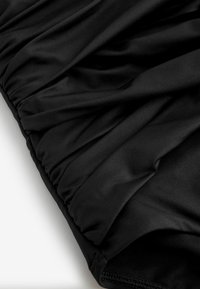 Material negru cu bandă elastică în talie, cu detalii adunate și drapate și textură netedă, prezentat într-o vedere de aproape.