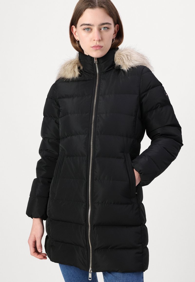 Zwarte gewatteerde winterjas met een bontvoering in de capuchon, ritssluiting en zijzakken. Heeft een gegolfde textuur en lange mouwen.