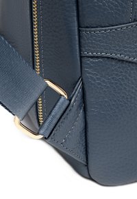 Navyblauwe leren tas met een gestructureerde afwerking, voorzien van een gouden rits en een bijpassende verstelbare schouderband. Metalen hardwareaccent op de schouderband.