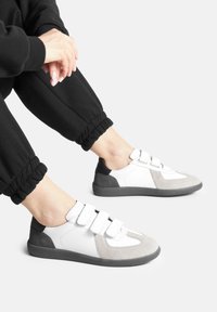 Valge, halli ja musta värvi Velcro tossud, millel on sametised ja siledad paneelid. Omab ümmargust varbaosa ja tekstureeritud kummist tallat.