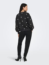 Black sweatshirt with white floral embroidery, relaxed fit, ribbed cuffs, paired with black tapered pants and heeled ankle boots.