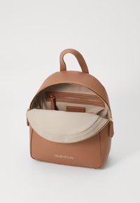 Hnědý kožený batoh se zipovým uzávěrem, béžovou podšívkou, vnitřními kapsami a zlatým kováním. Má horní rukojeť a elegantní zaoblený tvar.