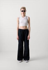 Chemise polo blanche courte avec un col et des rayures grises, assortie à un pantalon large noir taille haute avec de grandes poches et un cordon de serrage.