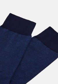 Temno modri pleteni rokavici z teksturirano površino in enobarvnimi rebrastimi manšetami, zasnovani za toploto in udobje.
