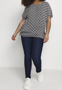 Haut gris avec un motif ondulé, manches courtes, coupe ample ; associé à un jean bleu foncé, coupe slim, et des baskets blanches.