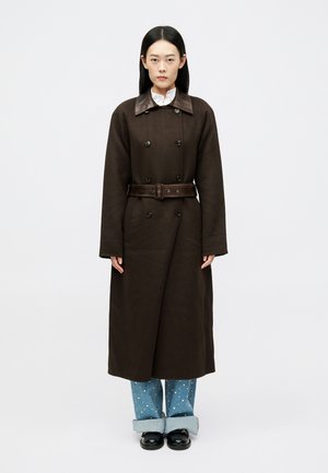 Rjav dvoredni plašč z usnjenim ovratnikom in usklajeno pasom, v kombinaciji s svetlo modrimi kavbojkami z belimi pikicami.