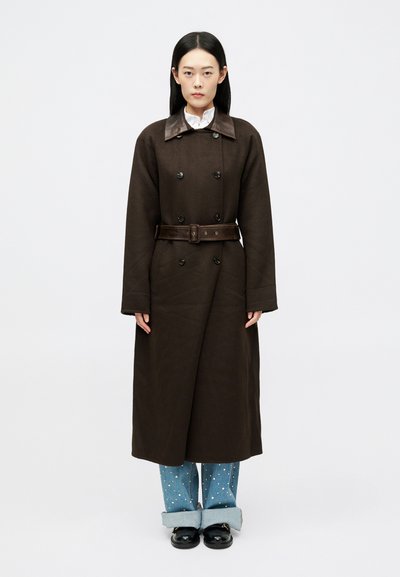 Brown double-breasted coat with a leather collar and matching belt, paired with light blue denim pants featuring white polka dots.