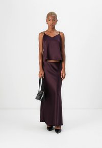 Mørkelilla sateng crop-topp og langt skjørt, med V-utringning og tynne stropper, kombinert med en liten svart håndveske og spisse hæler.