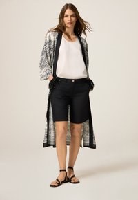 Shorts noirs associés à un blouse blanche, superposée avec un kimono à motifs présentant des designs noir et blanc et des accents en franges sur les manches.