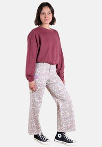 Sweatshirt bordeaux à épaules tombantes, associé à un pantalon évasé à motifs floraux clairs et des baskets montantes noires.