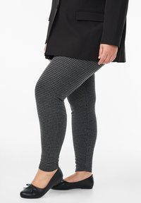 Melnbaltas houndstooth legingi, kas izgatavoti no elastīga materiāla, ar pieguļošu dizainu, kas pielāgojas kājām. Apvienoti ar melniem ķīlīšiem.