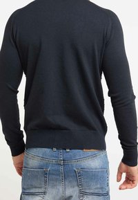 Tmavě modrý svetr s přiléhavým střihem, dlouhými rukávy, žebrovanými manžetami a lemem, vyrobený z hladkého materiálu. Nesen s světle modrými džíny.