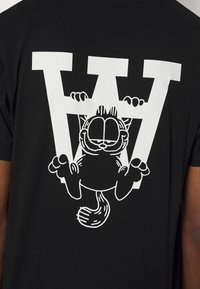 Black t-shirt featuring a large white graphic of a cartoon cat hanging from the letter "W" with distinct facial features and paws.
