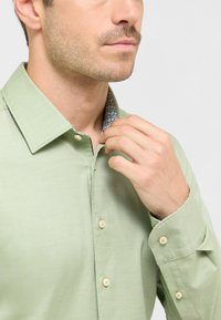 Lichtgroen button-up shirt met een gestructureerde afwerking, voorzien van een patroon in de kraagvoering en subtiele knoopdetails.