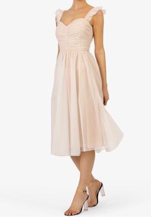 Abito rosa chiaro con spalline a volant, corpetto arricciato e gonna trasparente a pois lunghezza ginocchio. Sandali con tacco trasparente completano il look.