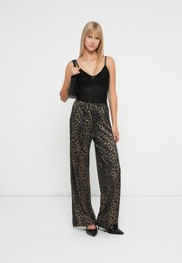 Femeie îmbrăcată cu un top negru fără mâneci, pantaloni largi cu imprimeu leopard strălucitor, tocuri negre și purtând o geantă de umăr neagră.